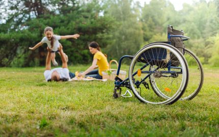 Disabled man out of his wheelchair lifting up his daughter in air at family picnic