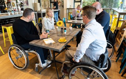three male wheelchair users meeting colleague from SIA around table in cafe
