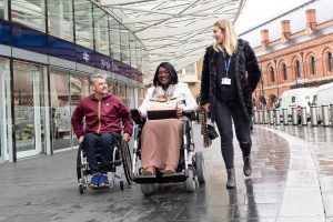 Two wheelchair users at Kings Cross train station on rainy day in London