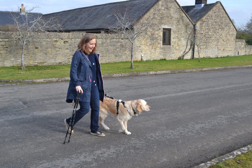 Lady walking her dog in countryside. Holding lead in left hand and walking stick in right hand