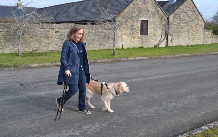 Woman walking with dog in countryside holding stick in right hand
