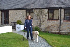 Lady with spinal cord injury walks dog along gravel path holding walking stick