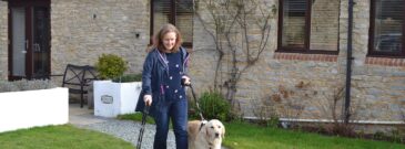 Lady with spinal cord injury walks dog along gravel path holding walking stick