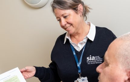 SCI Nurse talks with patient laid in bed about the support offered by charity