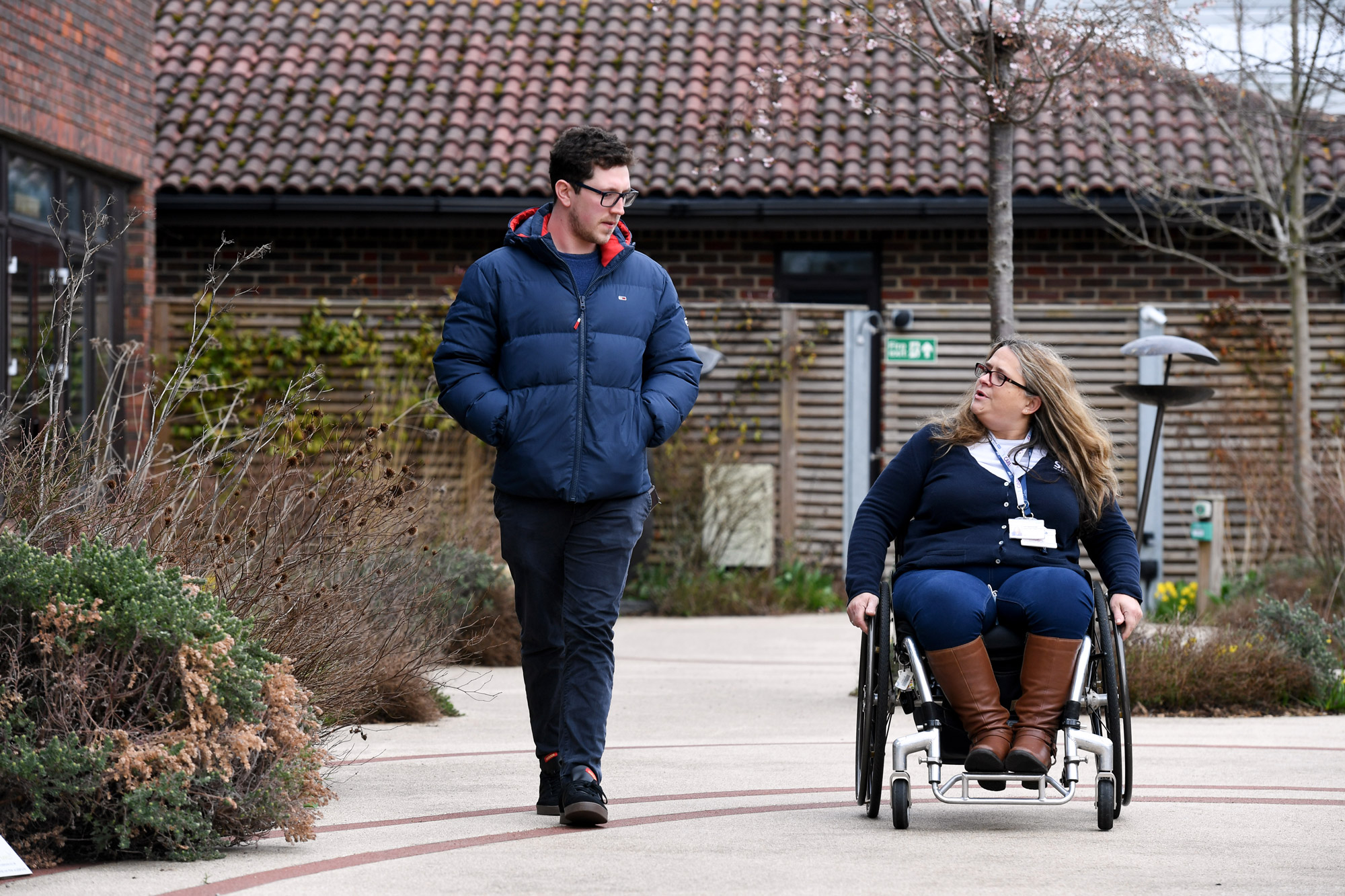 woman in wheelchair with man walking and talking at Stoke Mandeville