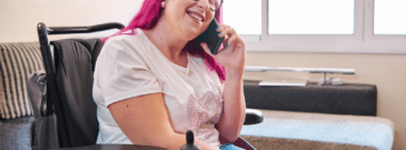 counselling - a female powered wheelchair user with pink hair on the phone and smiling (stock image)