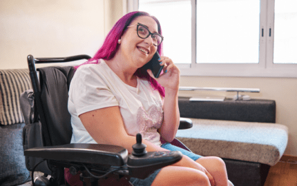 counselling - a female powered wheelchair user with pink hair on the phone and smiling (stock image)