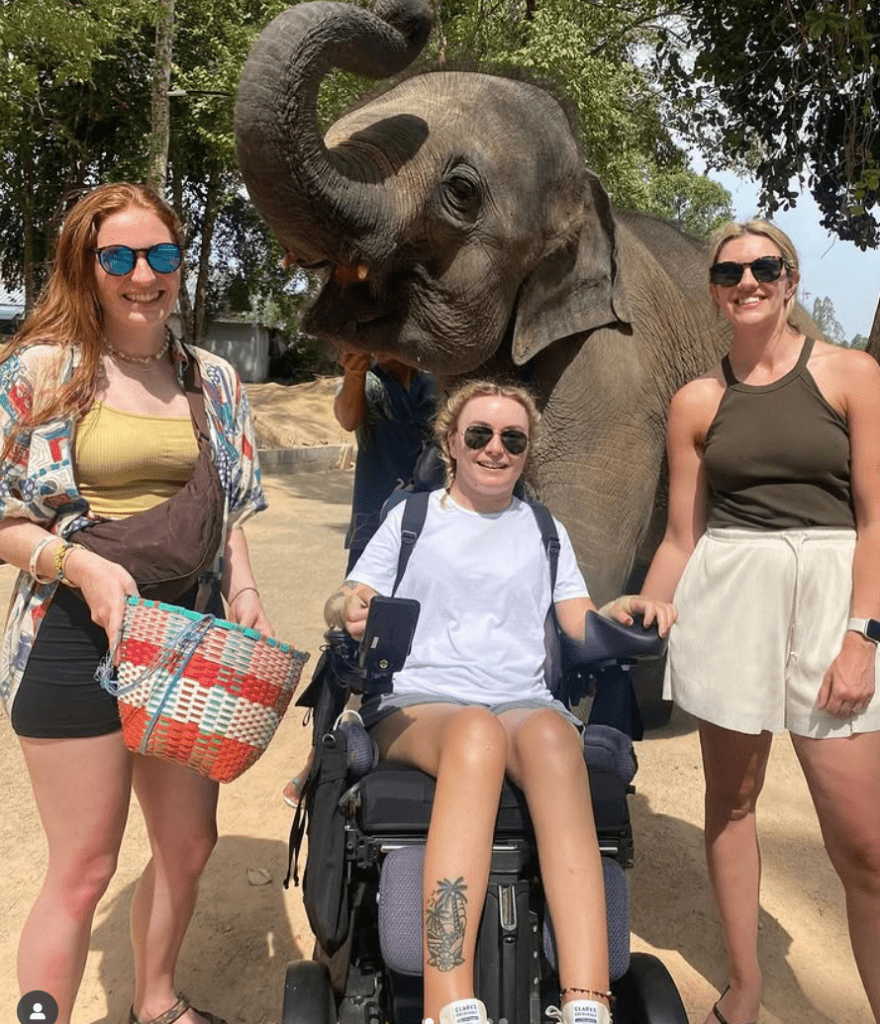 Rosie-Mayes in powered wheelchair holiday photo infront of elephant
