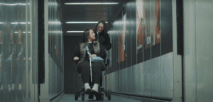 TWC video screenshot air travel. Disabled person pushed in wheelchair along corridor by airport staff member