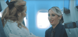 TWC video screenshot air travel. SIA member Jill talking to air stewardess whilst sat on plane seat