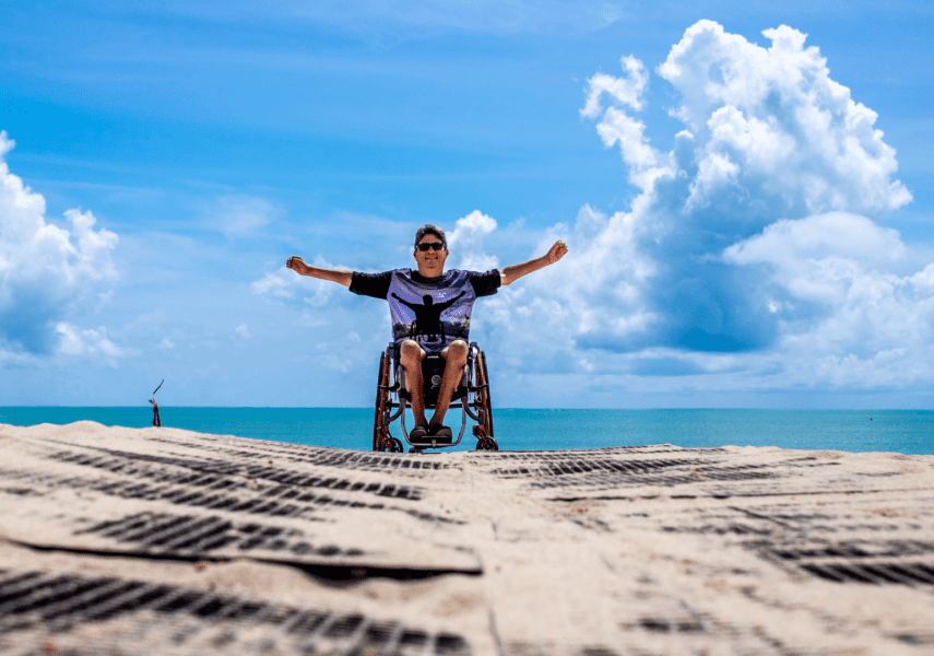 Beach wheelchair photo with wheelchair user with arms out wide on accessible slipway